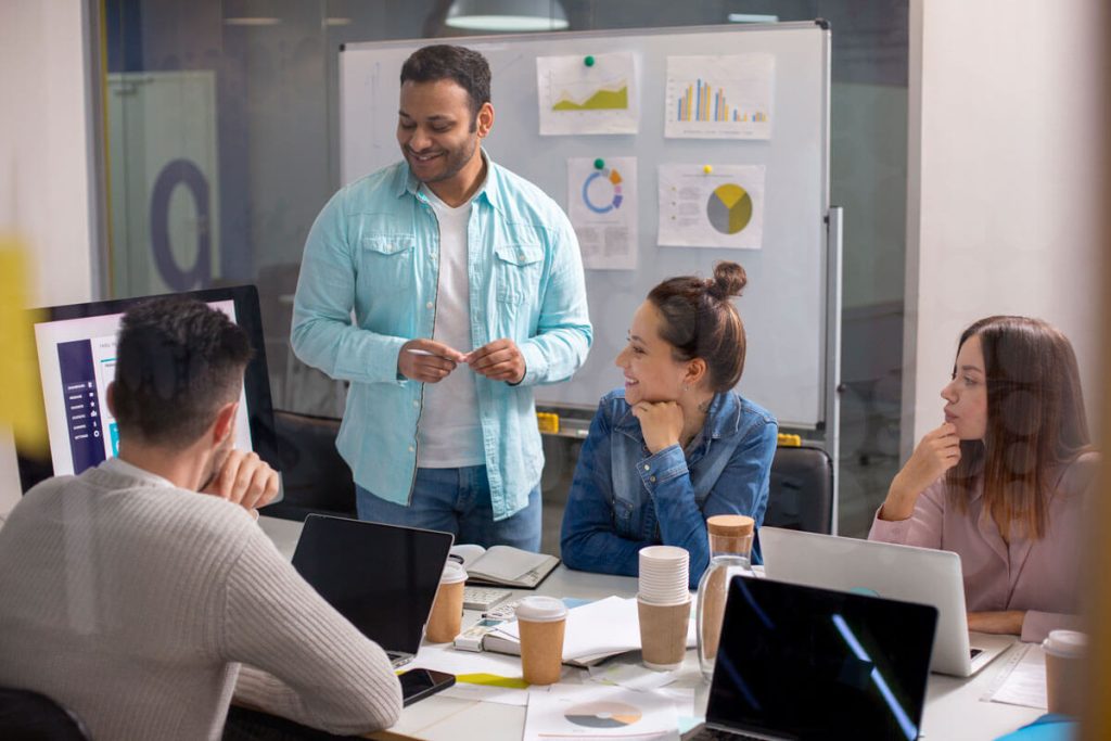 marketing-interno-vs-agencia-qual-escolher-capa-weein-agencia-de-marketing-digital-ot Equipe de marketing de 4 pessoas conversando em sala