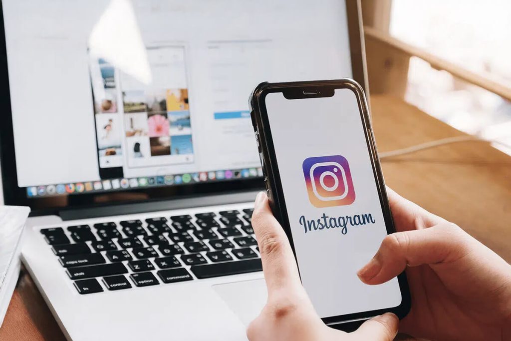 Instagram Profissional para Empresas: Transmita Confiança! Duas telas, notebook e celular, com pessoa mexendo no Instagram Profissional pelo celular